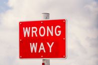 Clear image of a bright red 'Wrong Way' traffic sign against a cloudy sky in Miami, Florida.