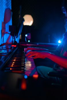 Moody shot of a person playing the piano in a dark studio with vibrant lighting.