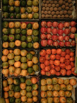 Top view of assorted fruits including oranges, pomegranates, and persimmons at a market stall.