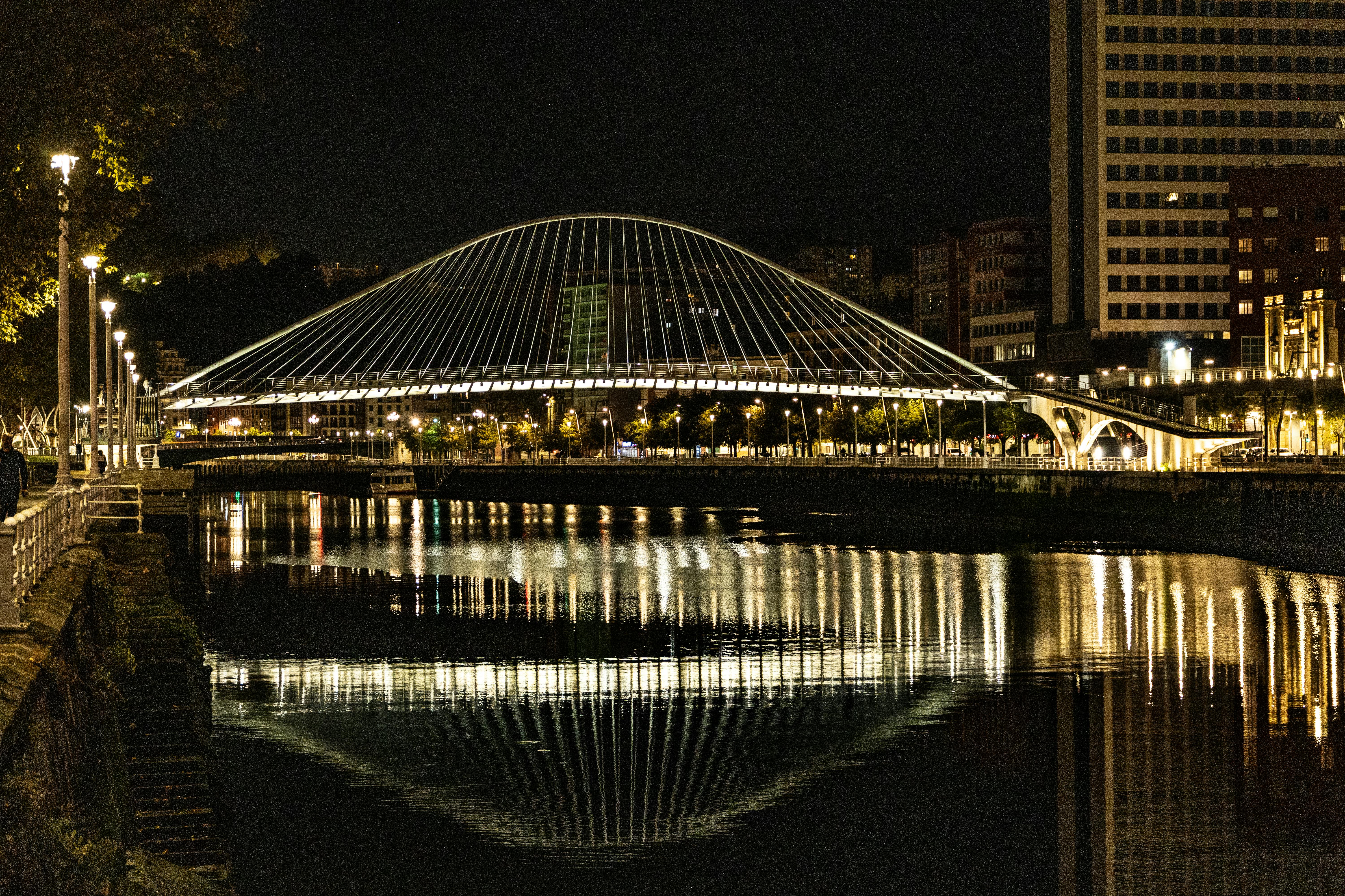 Night view of the illuminated Zubizuri Bridge in Bilbao reflecting in the river.
