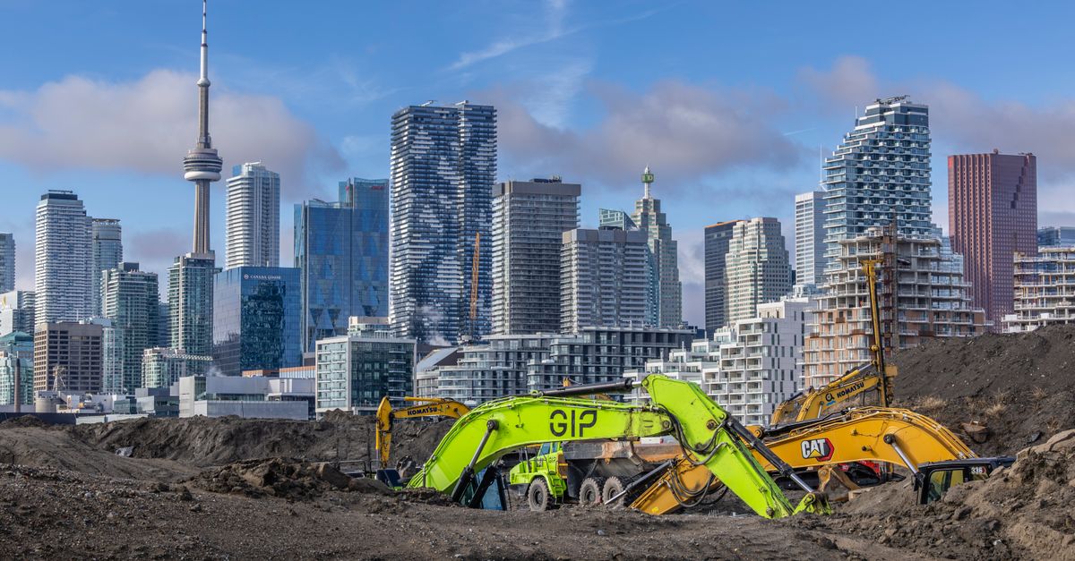 Excavators work at a Toronto construction site with the iconic CN Tower in the background.