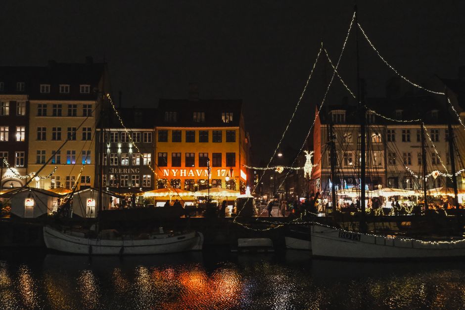Captivating night scene of Nyhavn Copenhagen with festive lights reflecting on the water.