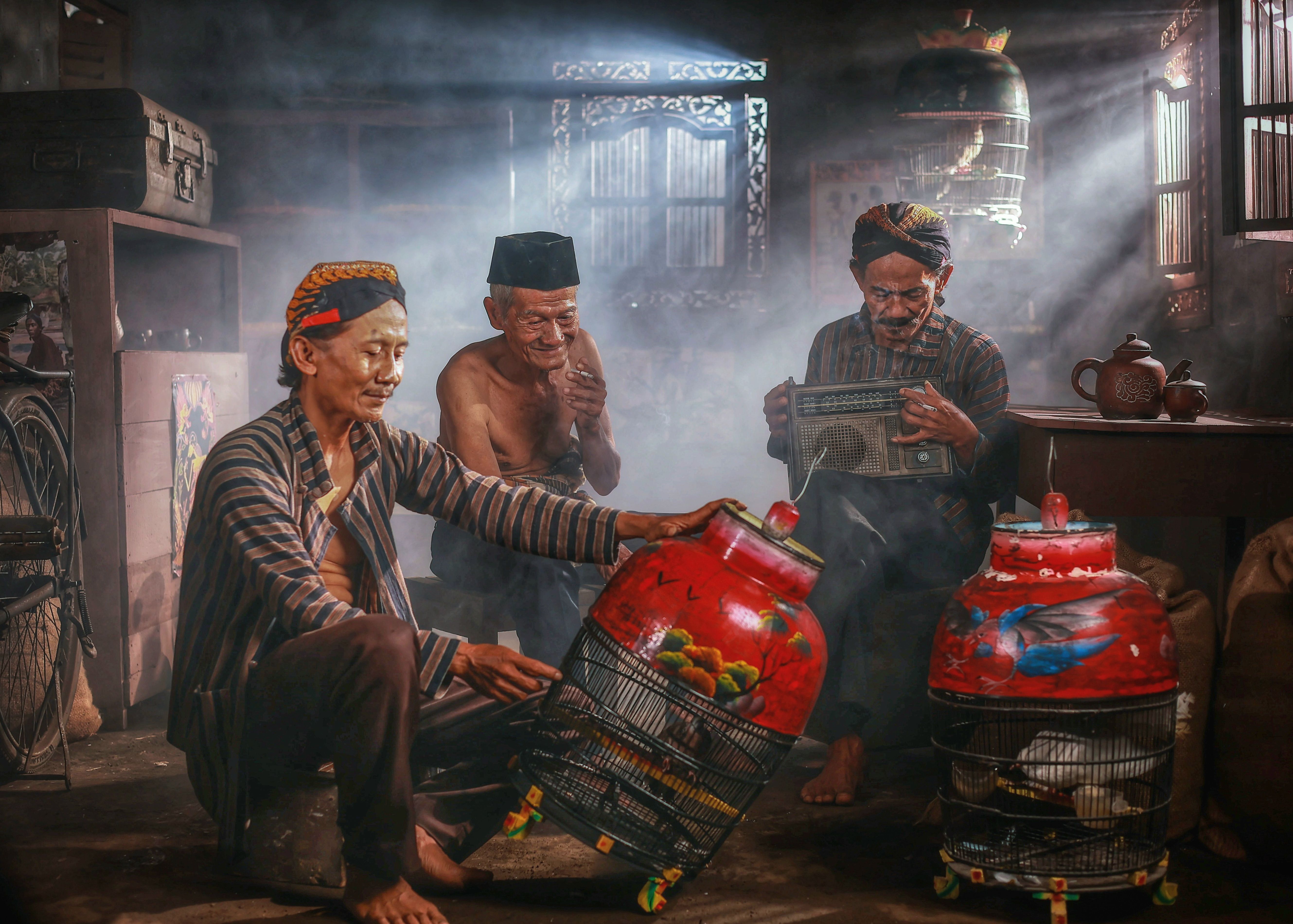 Three Javanese men enjoy bird keeping indoors, showcasing Indonesian culture in West Java.