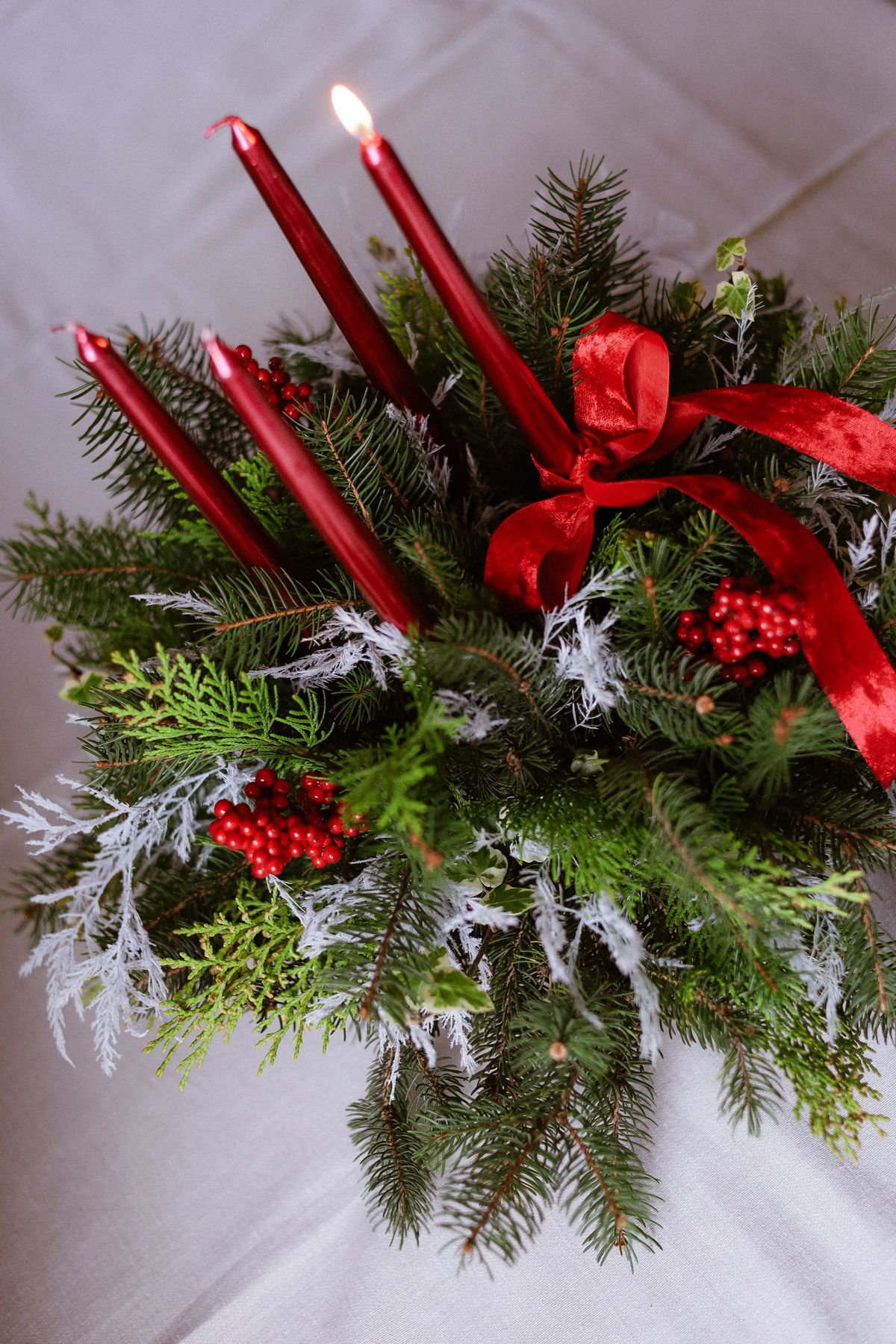 Elegant festive arrangement with red candles, greenery, and berries