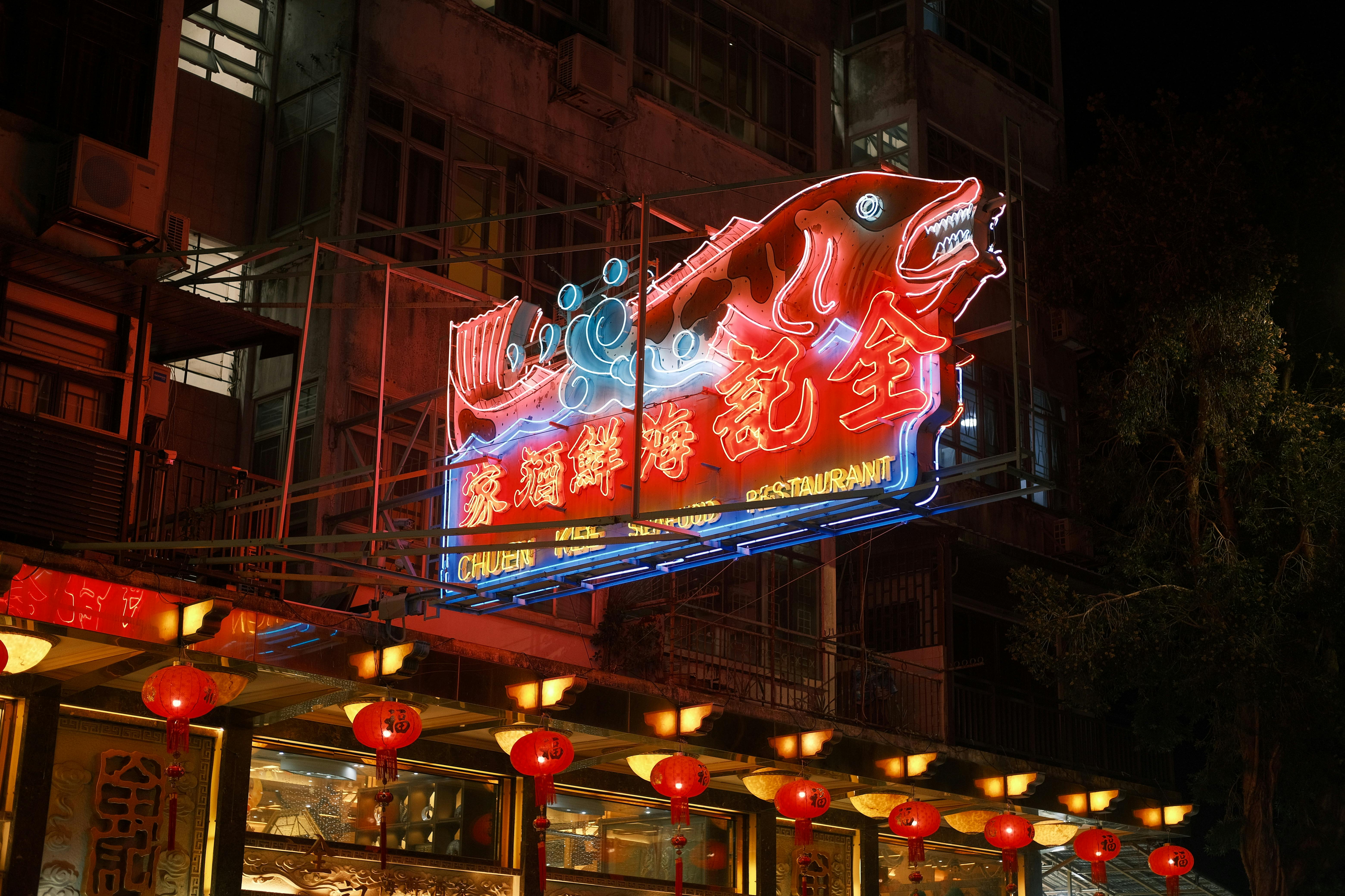 Illuminated neon sign in vibrant colors above a bustling Asian restaurant at night.