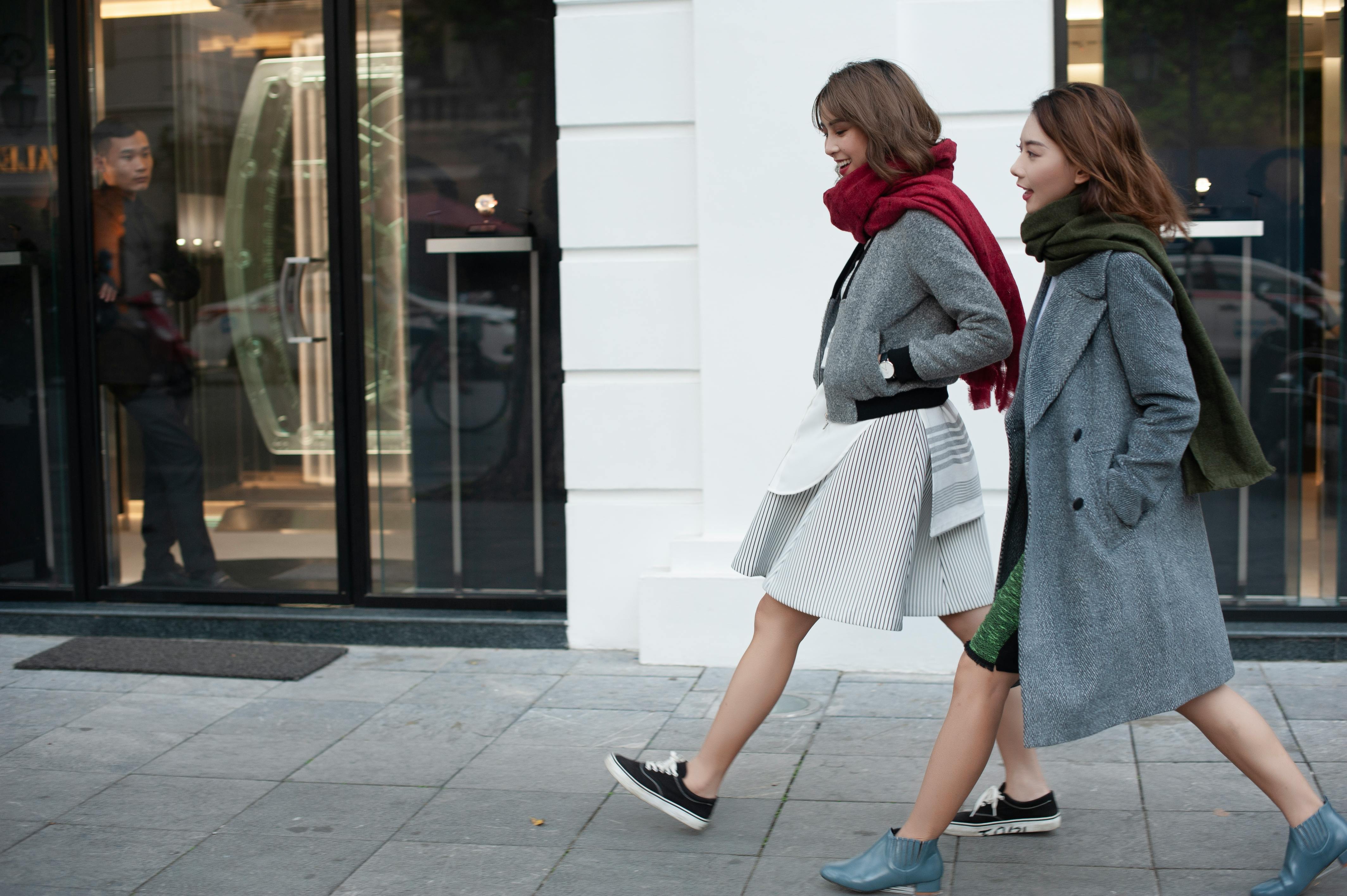 Two fashionable women walking past a store in an urban environment.