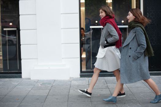 Two stylish women walking downtown in cozy coats and scarves on a chilly day.