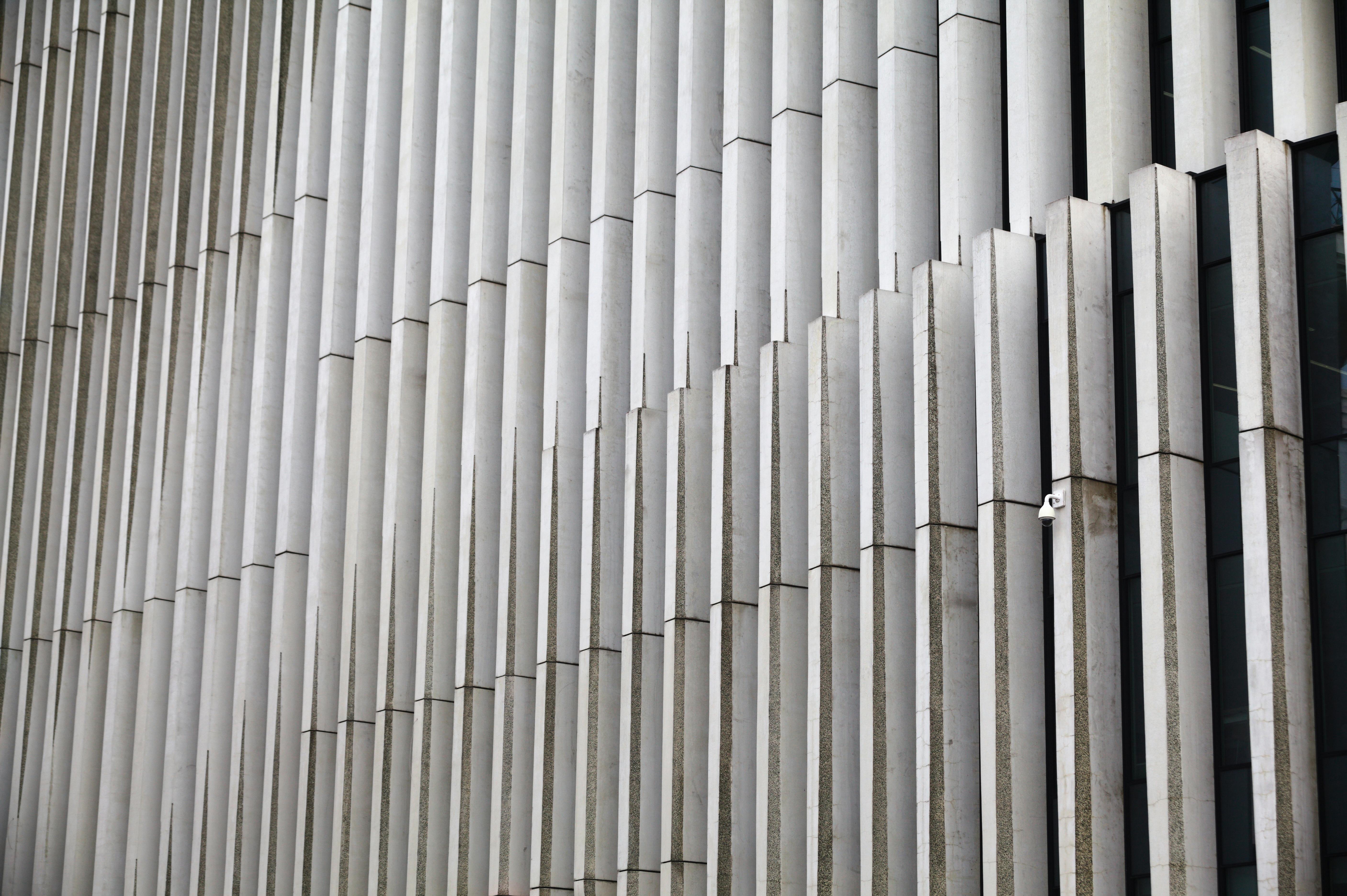 Symmetrical view of a modern building facade with vertical concrete panels and a security camera.