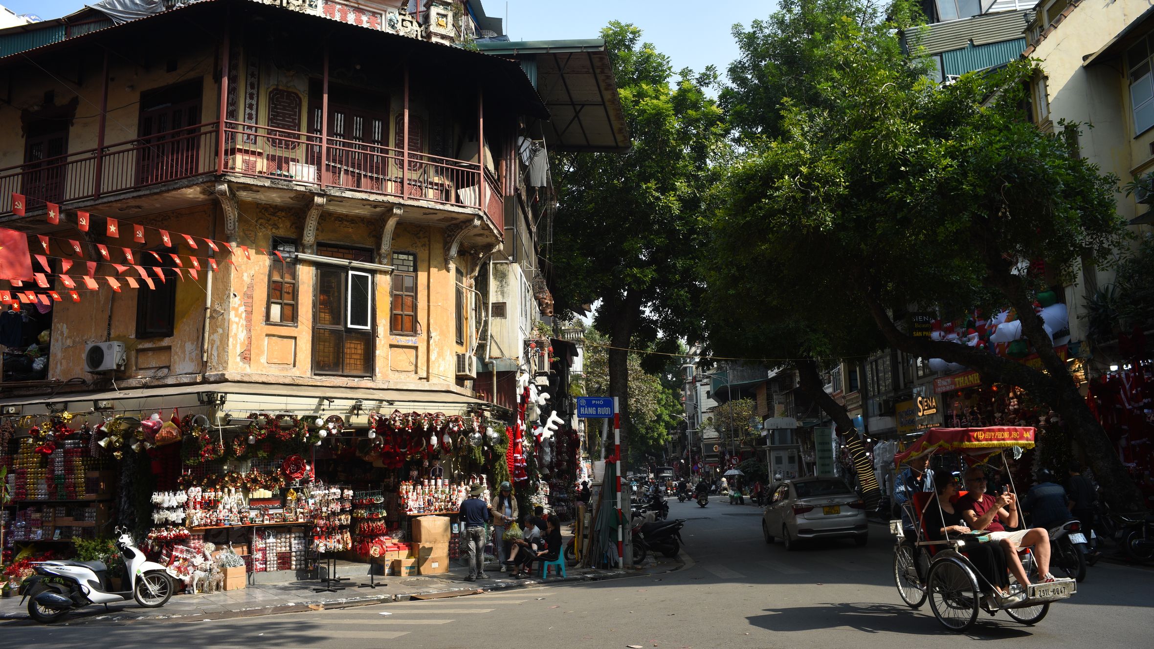 Lively street corner in Hanoi featuring traditional architecture and a passing rickshaw