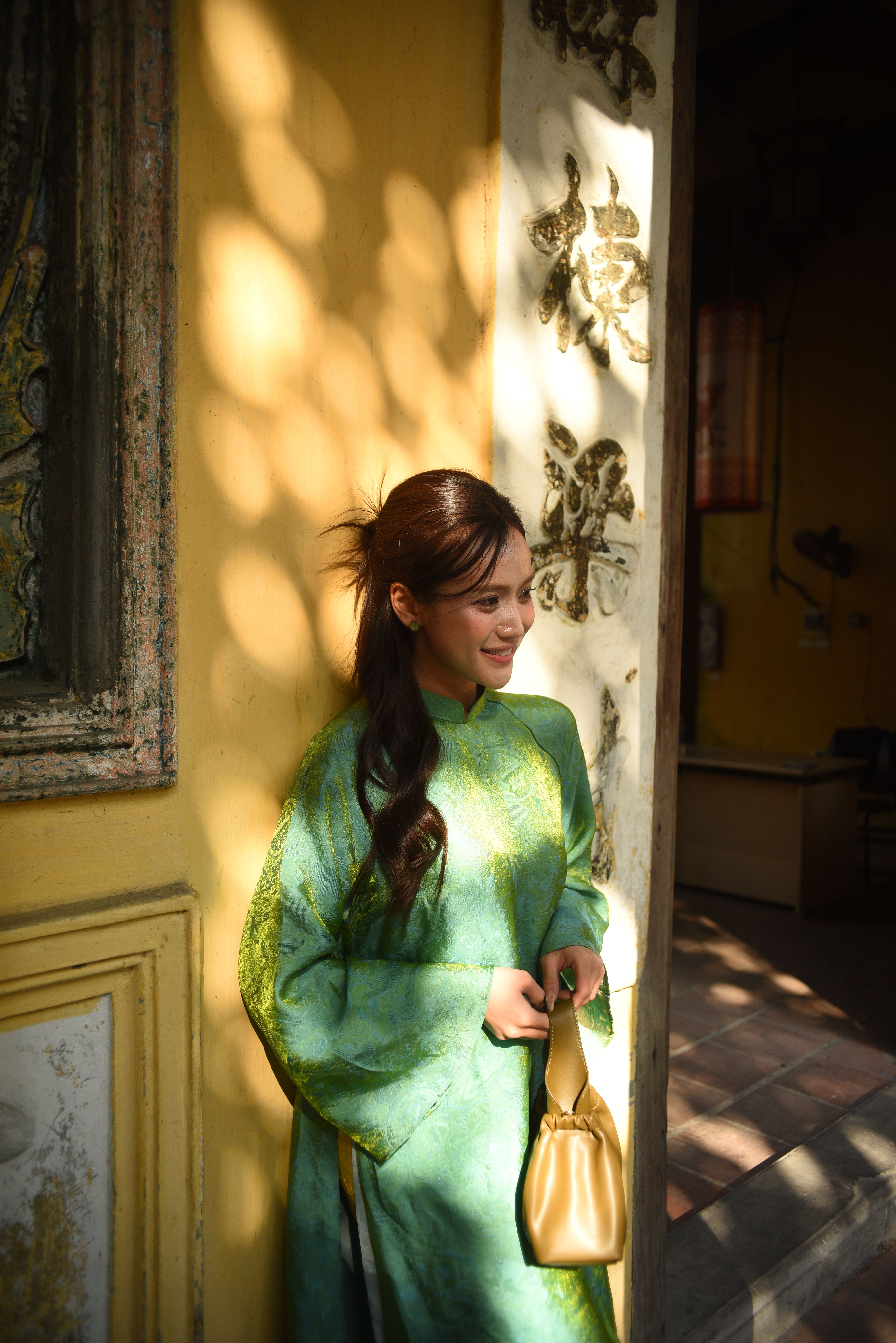 Smiling woman in green traditional dress standing in sunlit doorway of ornate building.