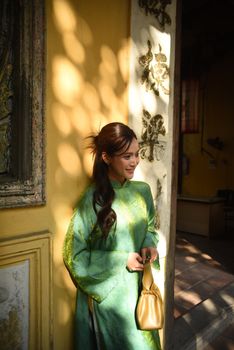 Smiling woman in green traditional dress standing in sunlit doorway of ornate building.