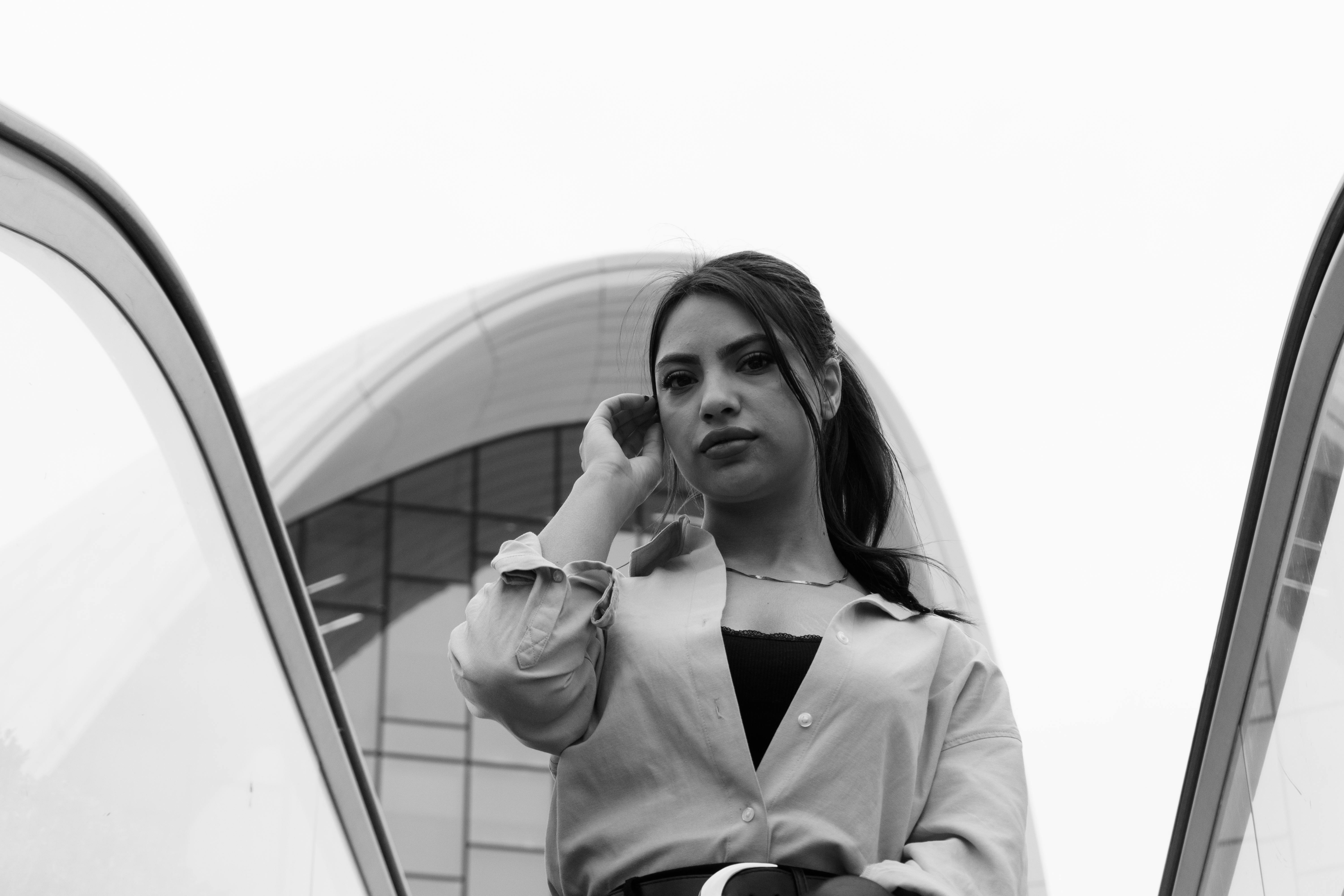 grátis Retrato em preto e branco de uma mulher em pé em frente a uma arquitetura moderna, conferindo um toque elegante e contemporâneo. Foto profissional