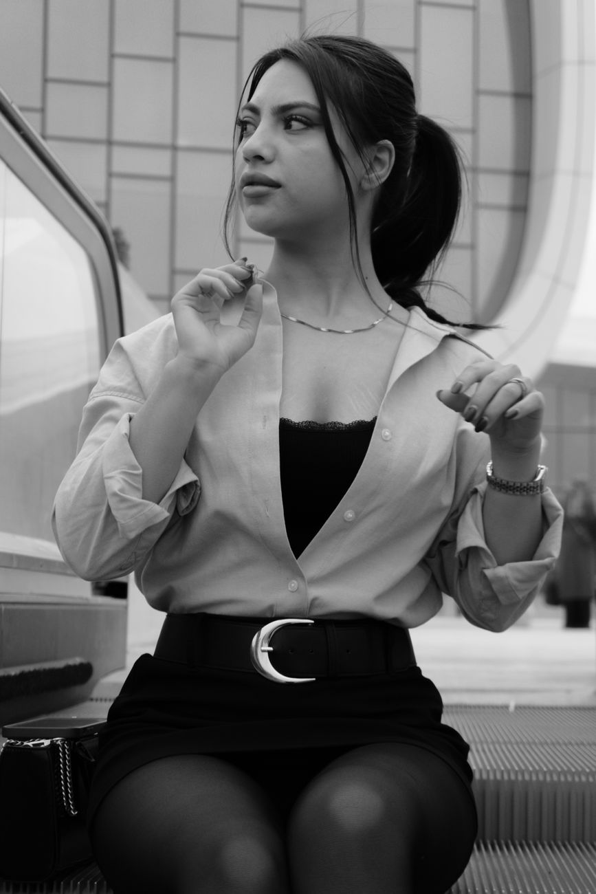 Black and white photo of a young woman sitting confidently in an urban environment.
