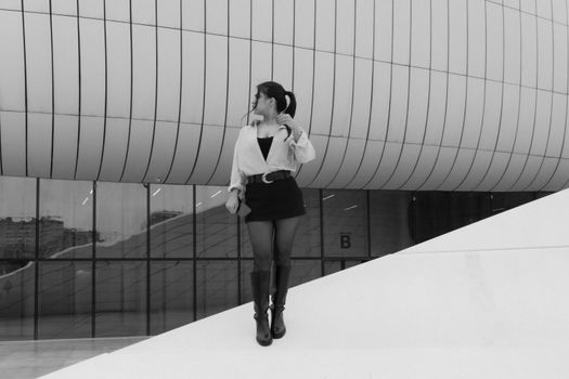 A woman standing against a modern architectural backdrop in black and white, exuding elegance.