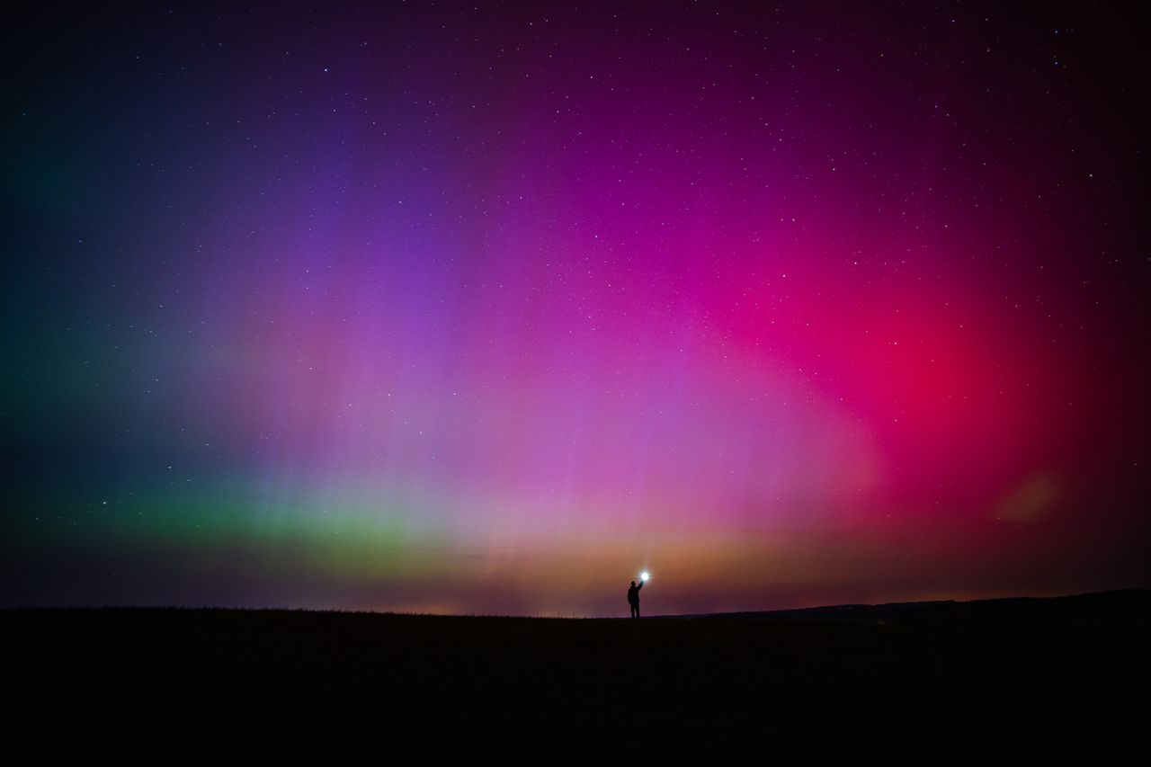 Pink and green aurora over a dark landscape with a tiny figure
