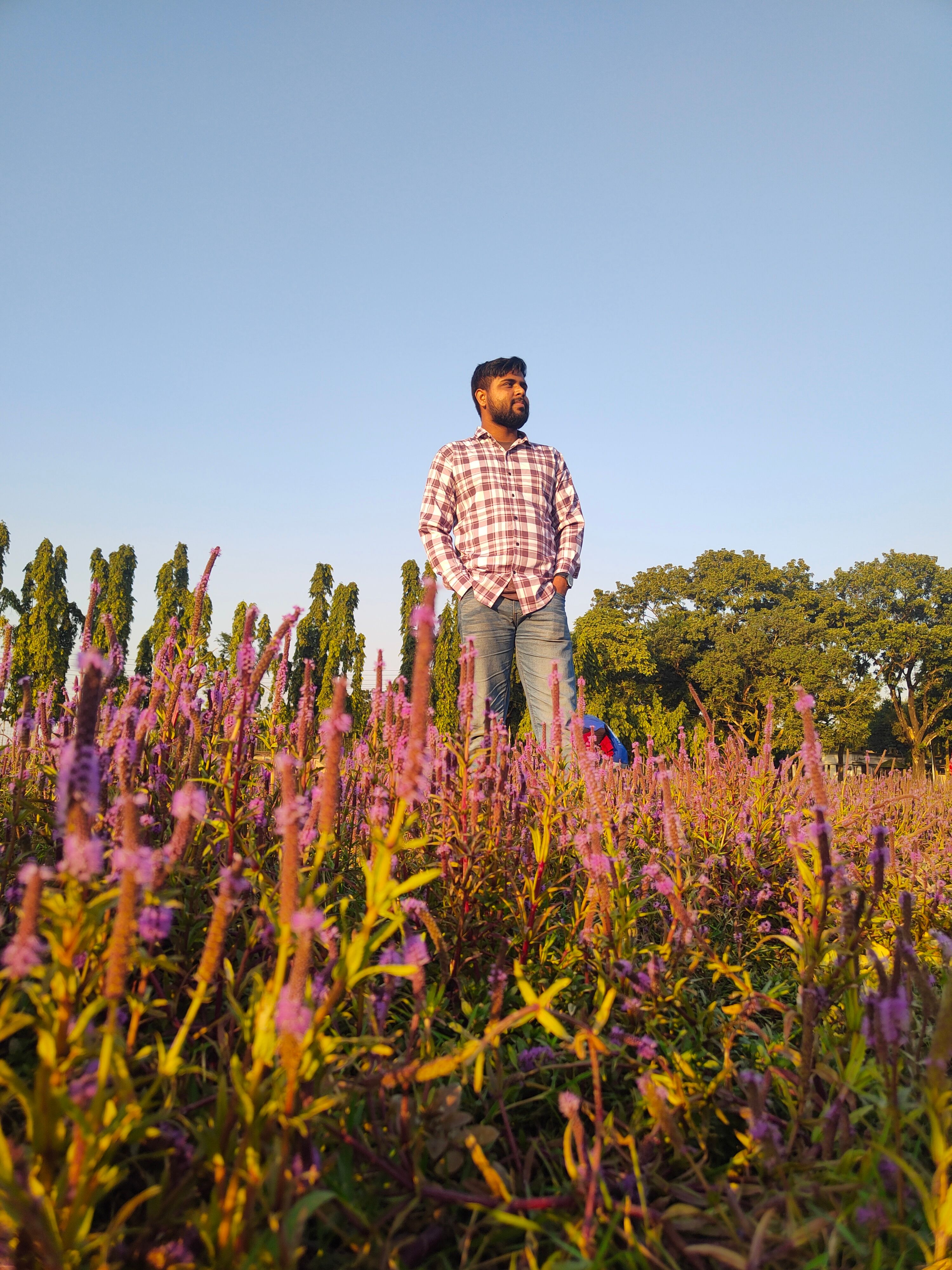 A man stands in a field of vibrant wildflowers during golden hour, conveying tranquility and nature's beauty.
