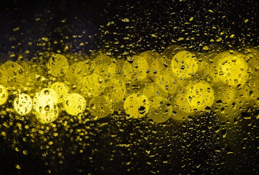 Raindrops on glass transform into an abstract pattern with golden bokeh lights, creating a moody and artistic atmosphere.