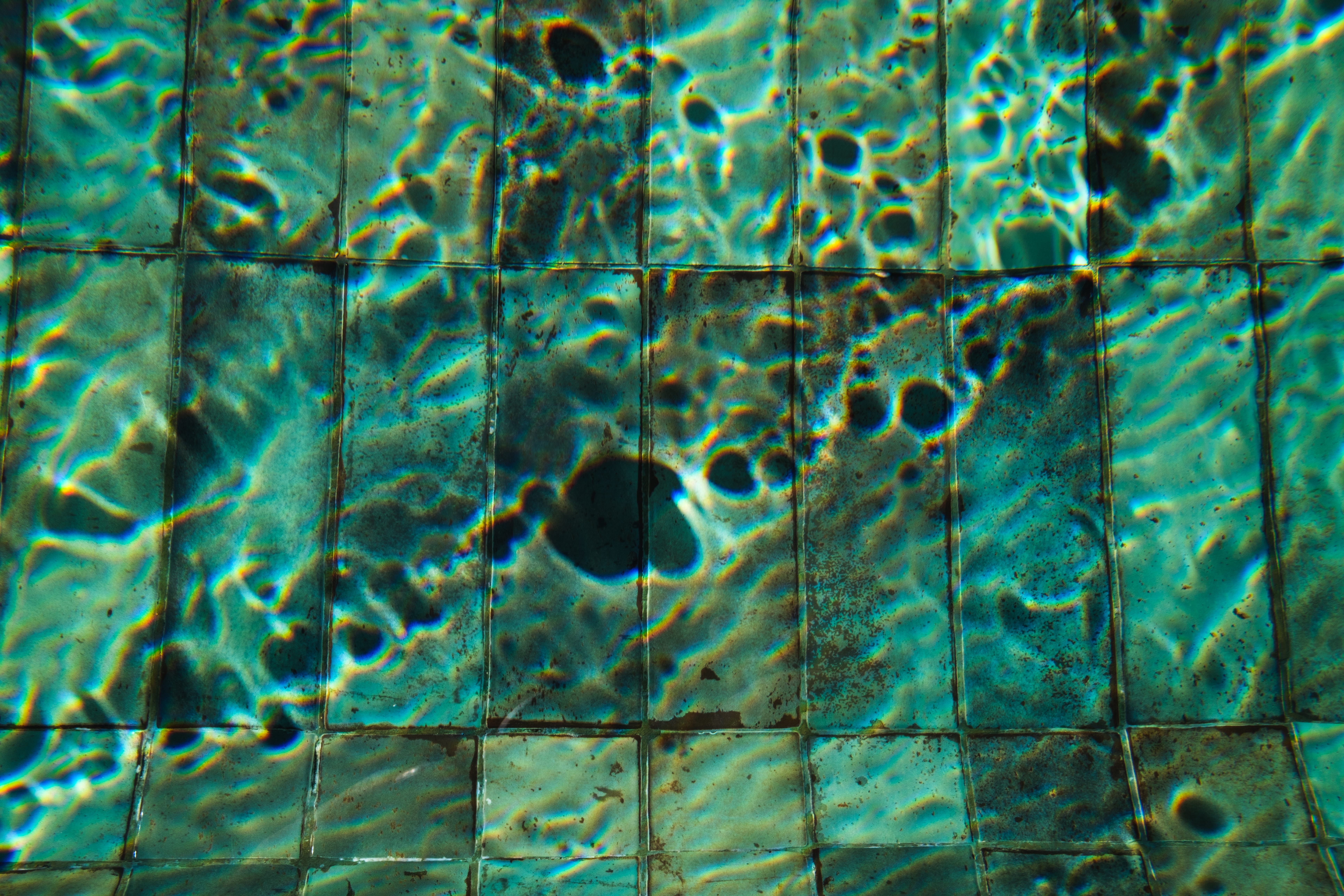 Abstract water reflections casting patterns on aged pool tiles, creating a vibrant visual display.