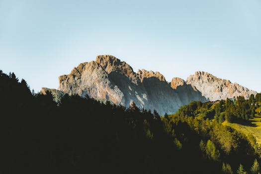 Breathtaking view of a sunlit mountain range with lush green forest in a serene landscape.