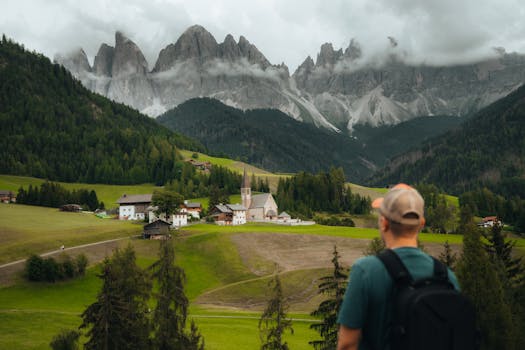 Traveler stands admiring the picturesque Dolomite mountains and quaint village below.