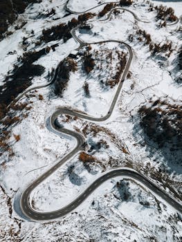 Aerial photo of a snowy serpentine road through mountains, showcasing winter scenery.