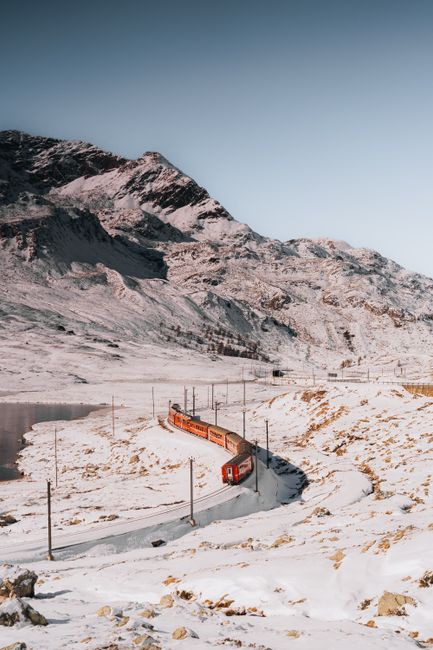 A red train travels through the snowy landscape of the Swiss Alps, showcasing breathtaking winter scenery.