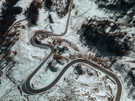 A winding road through snow-covered mountains showcases nature's beauty in winter from above.