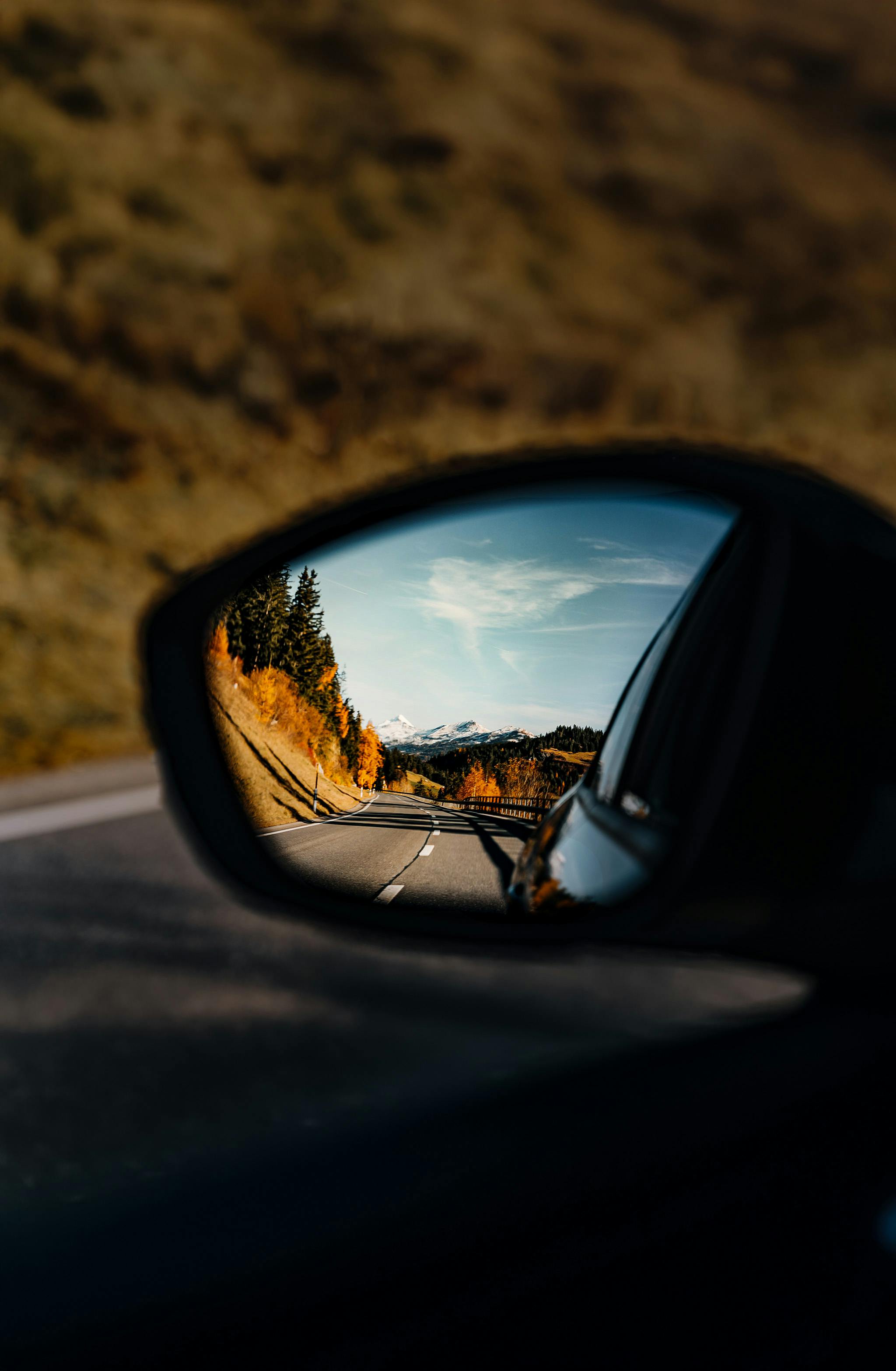 Serene autumnal landscape captured in a car's rearview mirror.