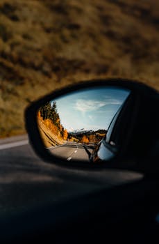Serene autumnal landscape captured in a car's rearview mirror.