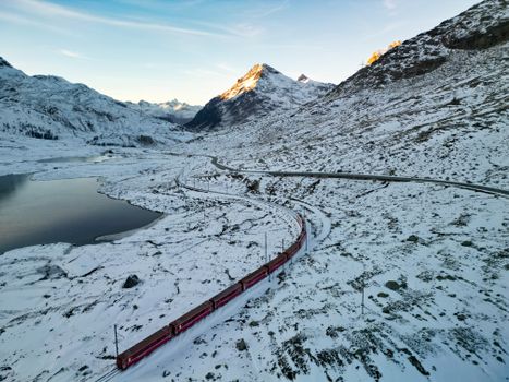 A red train travels through snowy Swiss Alps, showcasing stunning winter scenery.