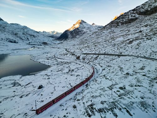 Free A red train travels through snowy Swiss Alps, showcasing stunning winter scenery. Stock Photo