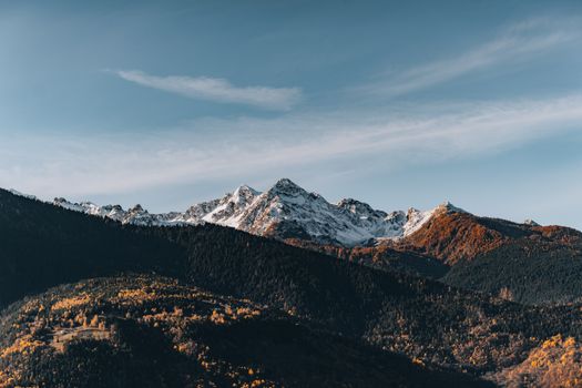 Breathtaking view of snow-capped mountains and autumn foliage under a clear blue sky.