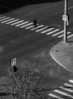 Monochrome aerial shot of a pedestrian crossing a city street intersection.