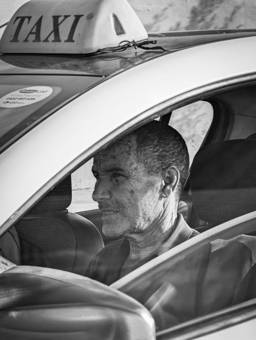 Free Black and white image of a taxi driver seated inside a vehicle, captured in profile. Stock Photo