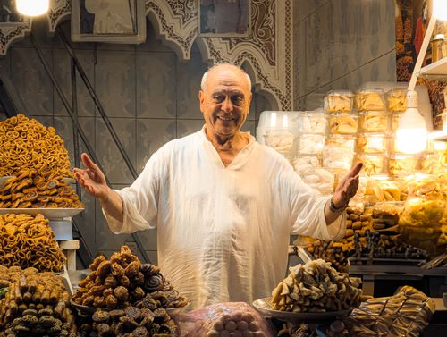 Free Elderly man in a traditional market stall surrounded by a variety of sweets and pastries. Stock Photo