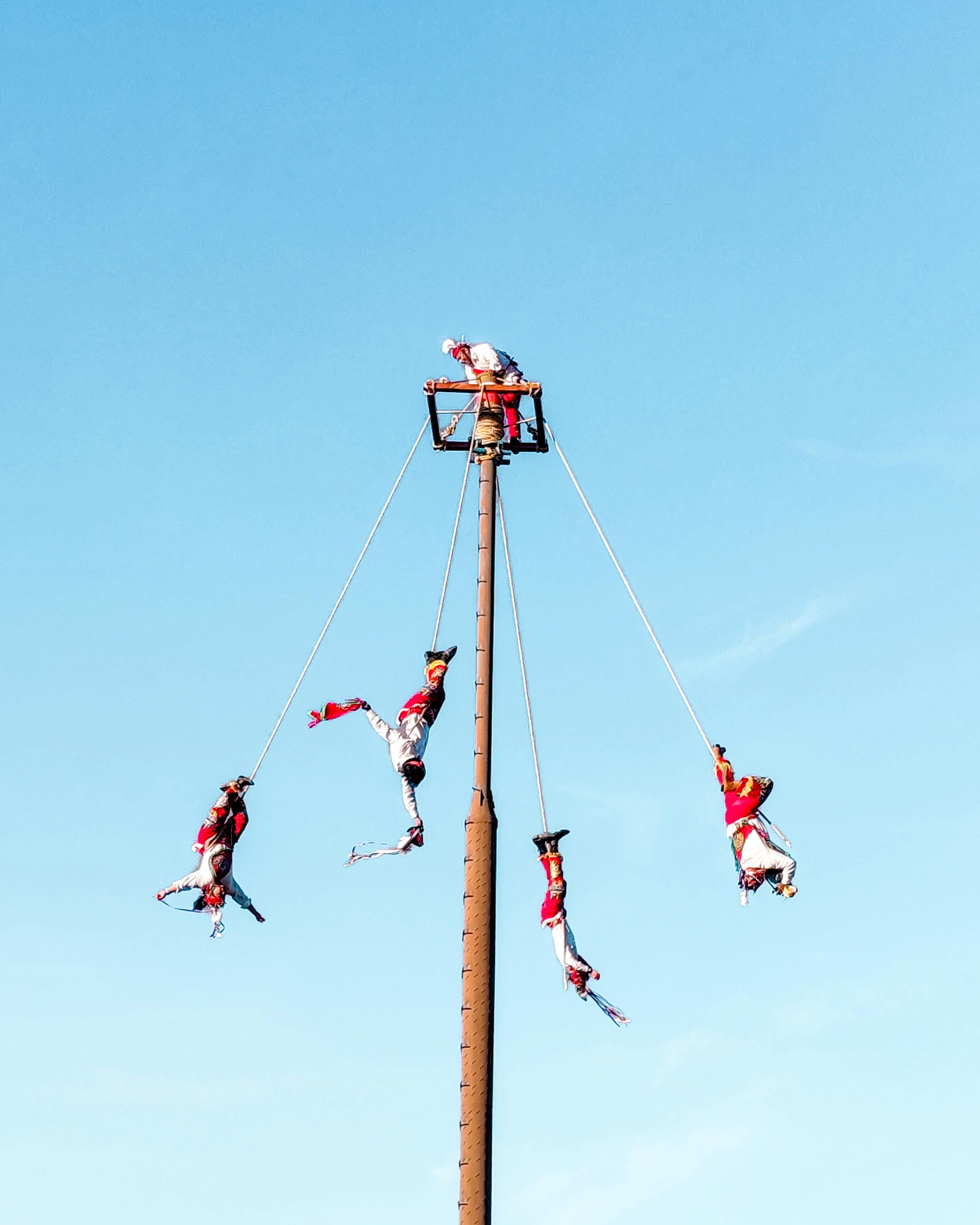 Performers executing a traditional flying dance on poles against a clear sky.