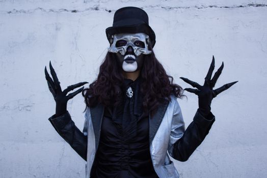 Mysterious figure in silver and black costume with skeletal mask and top hat.