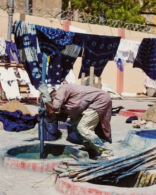 Free An artisan skillfully dyes fabrics outdoors under the bright African sun. Stock Photo