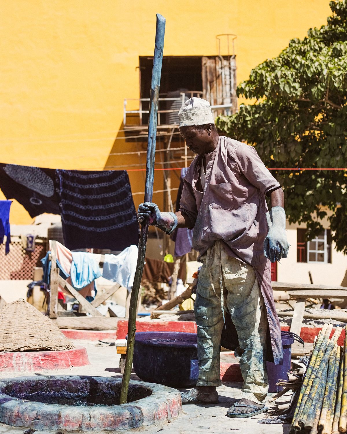 A dyer stirring an indigo pit, with dyed cloth drying in the sun