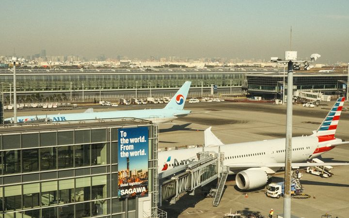 Aerial view of a bustling airport tarmac with parked airplanes and terminal building under clear skies.