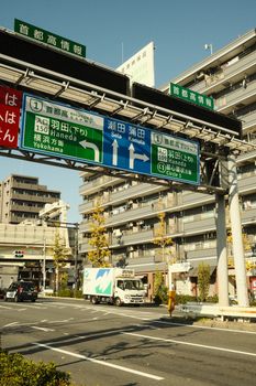 Japanese road signs with urban high-rise buildings in the background, captured in daylight.