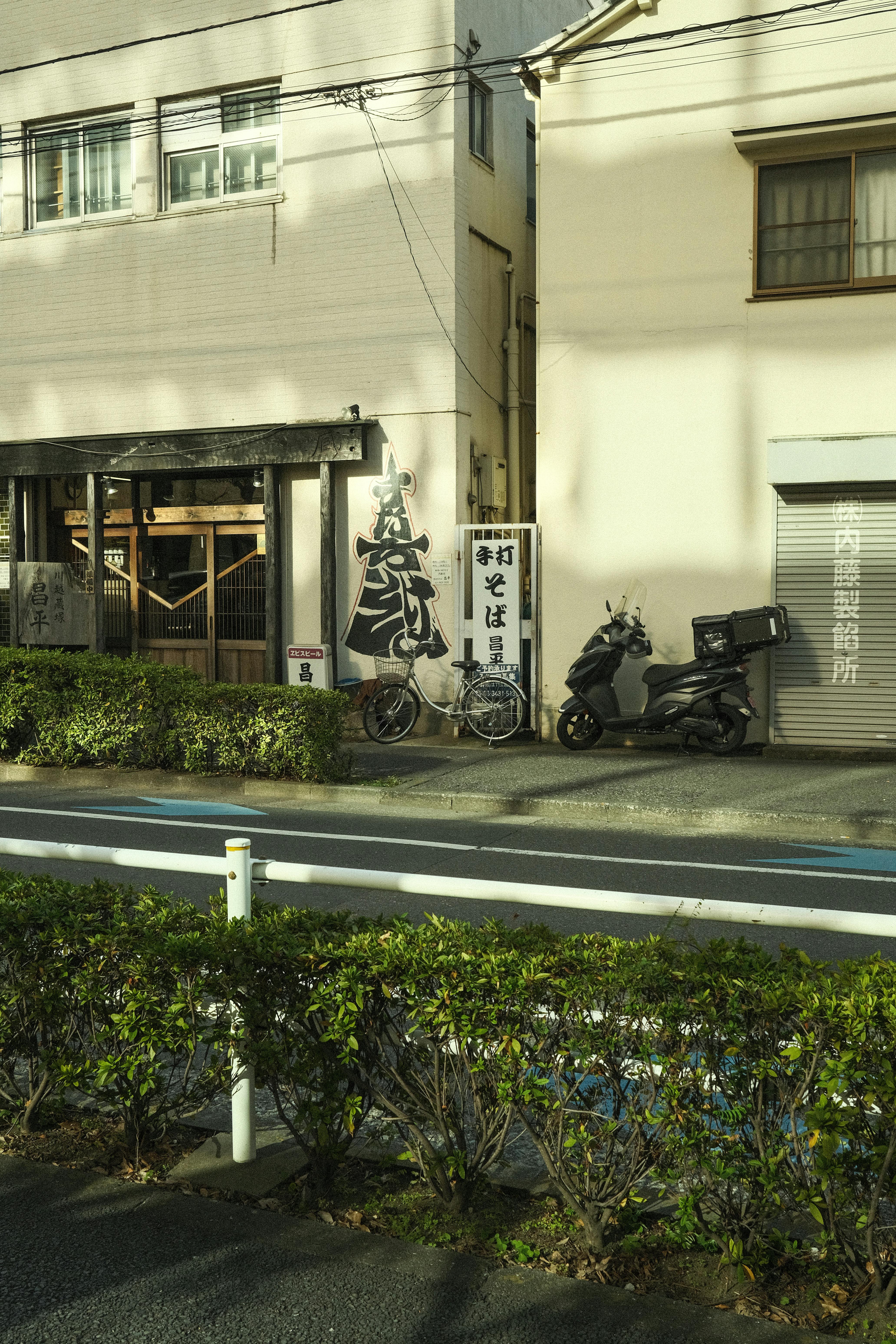 Urban Japanese street scene with bicycles, scooters, and traditional sign next to a building.