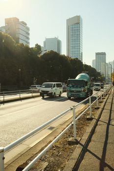 Traffic on a city road with skyscrapers and trees, showcasing a busy urban morning.