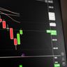 A dark digital screen displaying a candlestick chart with a sharp red downward trend.