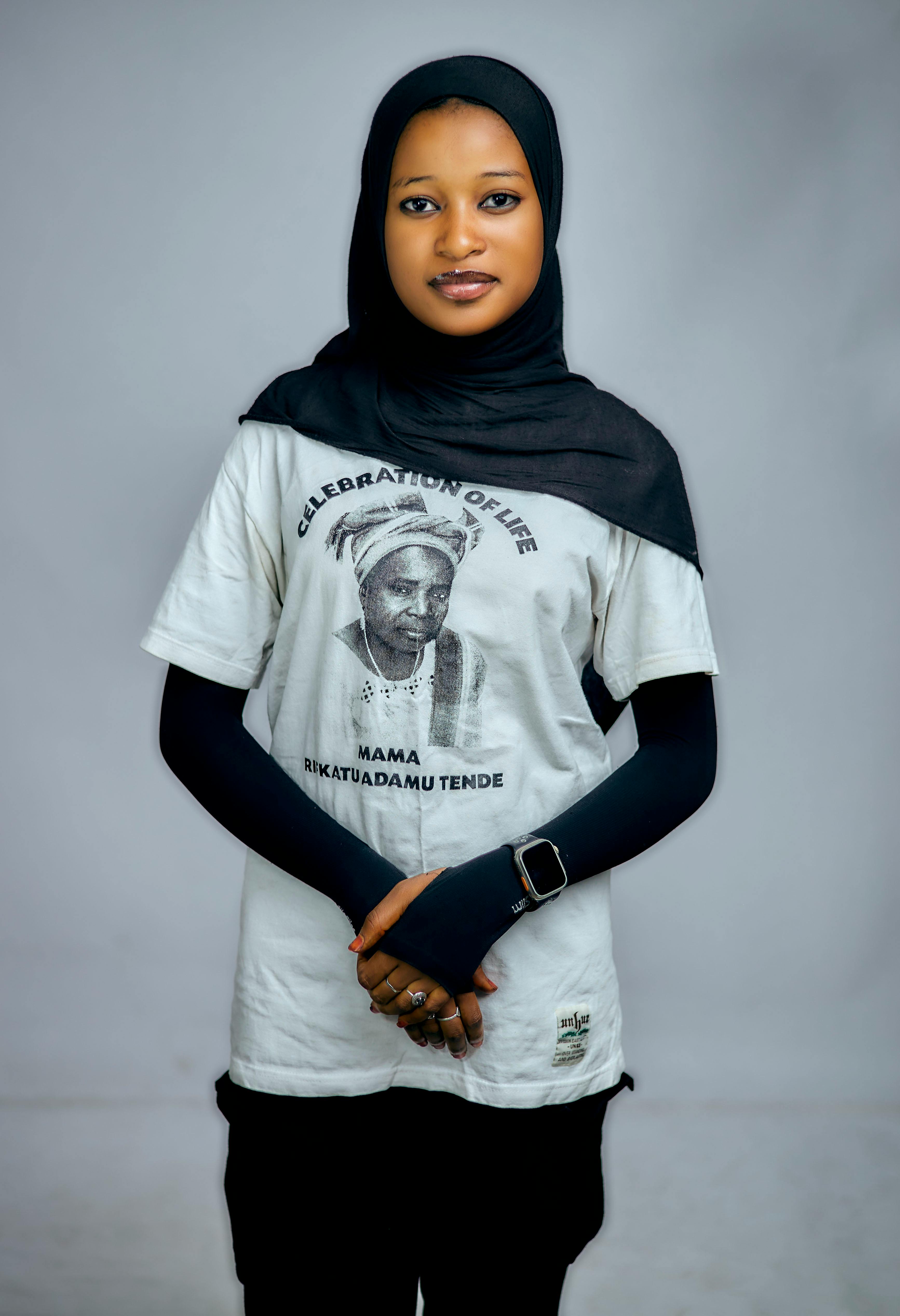Portrait of a young Muslim woman in hijab, wearing a tribute shirt indoors.