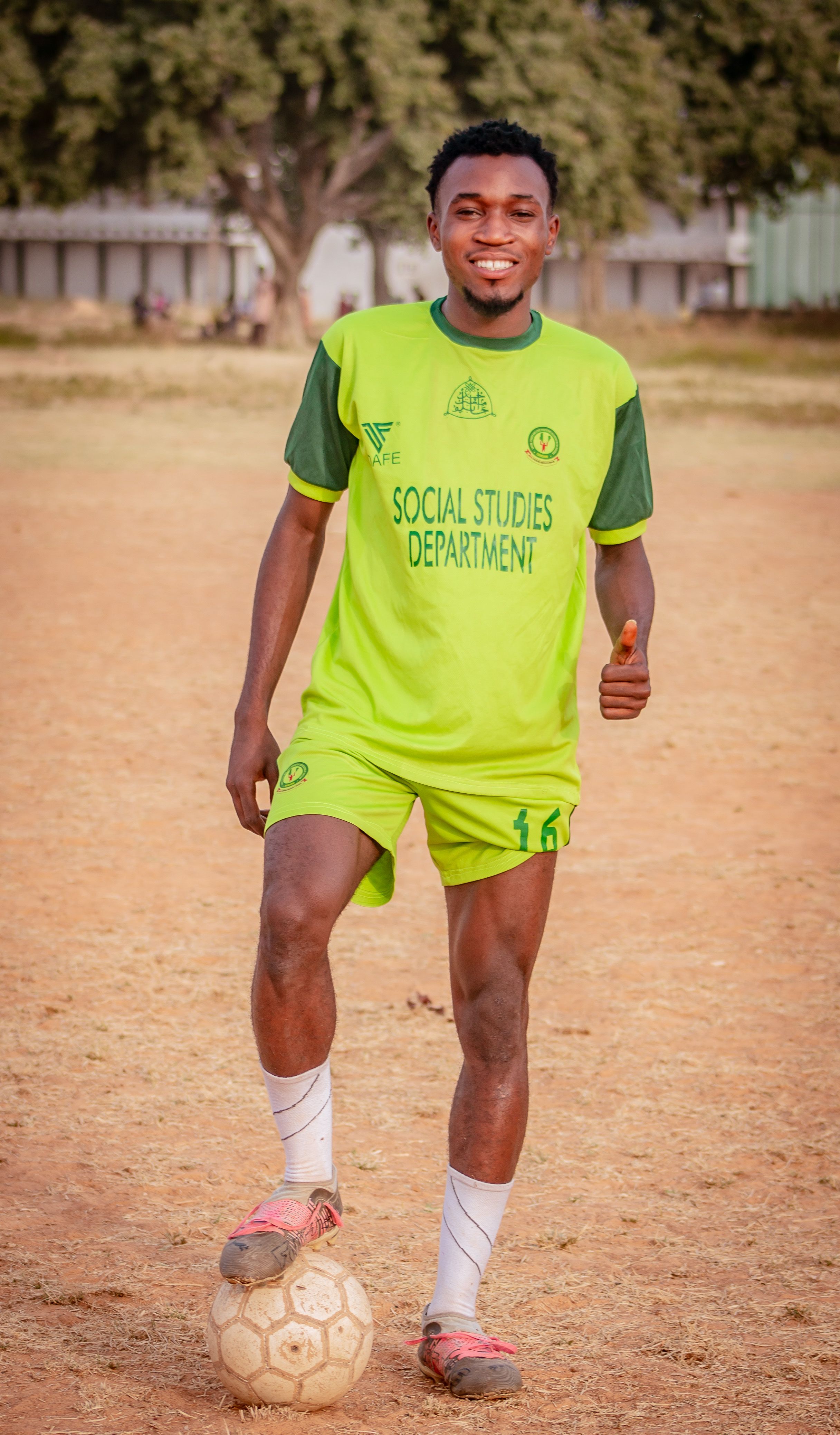 Smiling young male football player in a green uniform poses on a sunny field.