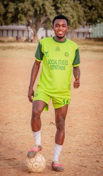 Smiling young male football player in a green uniform poses on a sunny field.