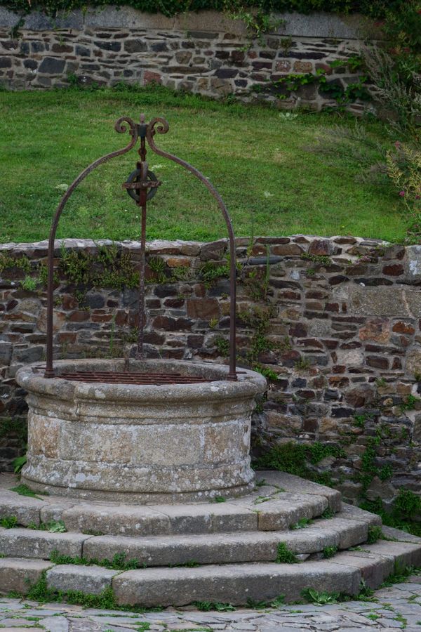 Vieux puits en pierre avec potence en fer forgé et poulie contre un mur de moellons