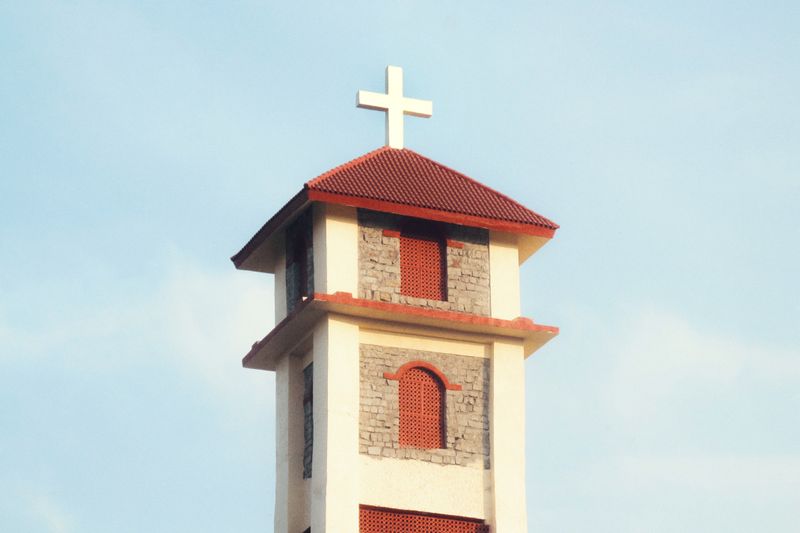 A church bell tower with a red roof and cross against a clear blue sky.