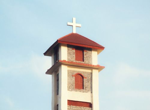Free A church bell tower with a red roof and cross against a clear blue sky. Stock Photo